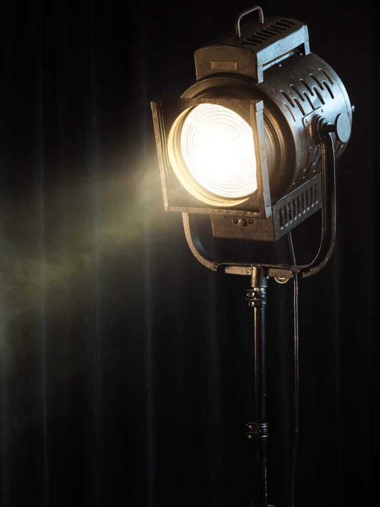 A lit spotlight stands before a curtain with smoke drifting in the light.