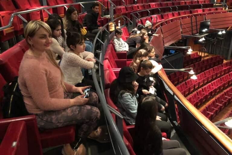 Children sit in the auditorium with their group leader, ready to watch a performance.