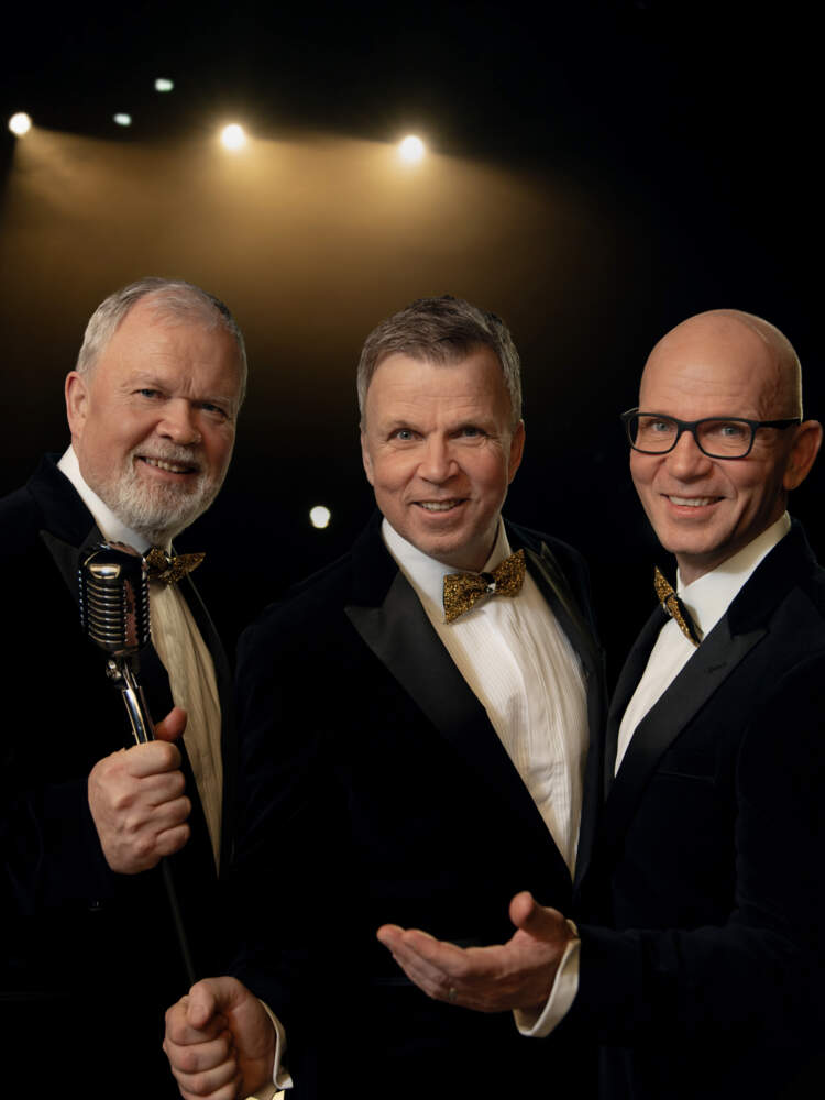 Tre leende bröder står upplyst på en mörk scen. De diggar faktumet att ett par gyllene dojor står och blixtar bakom kameran.