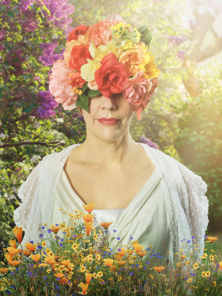 En person som bär en huvudbonad täckt av färgglada blommor står bland blommor i en solig, frodig trädgård.