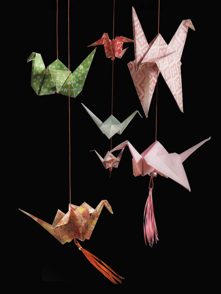 Sju färgglada papperstranor hänger från röd sidentråd. De hänger på olika höjd.