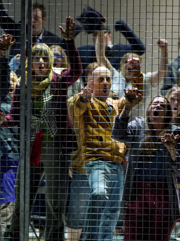 Många politiska fångar står bakom ett metallstängsel, några som greppar nätet med händerna. De sjunger på hög volym.