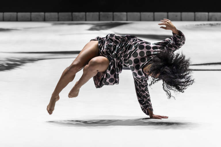 En dansare balanserar med ena handen på golvet och trycker iväg med båda benen böjda och i luften.