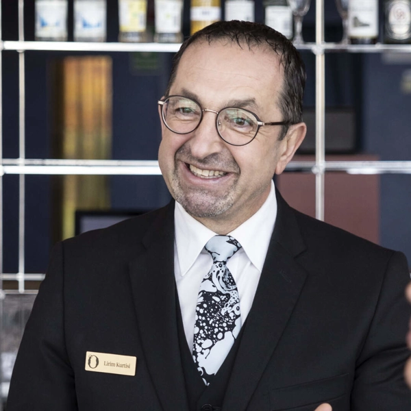 En leende caféchef pratar med två kunder som står vid cafédisken och köper kaffe och något att äta.