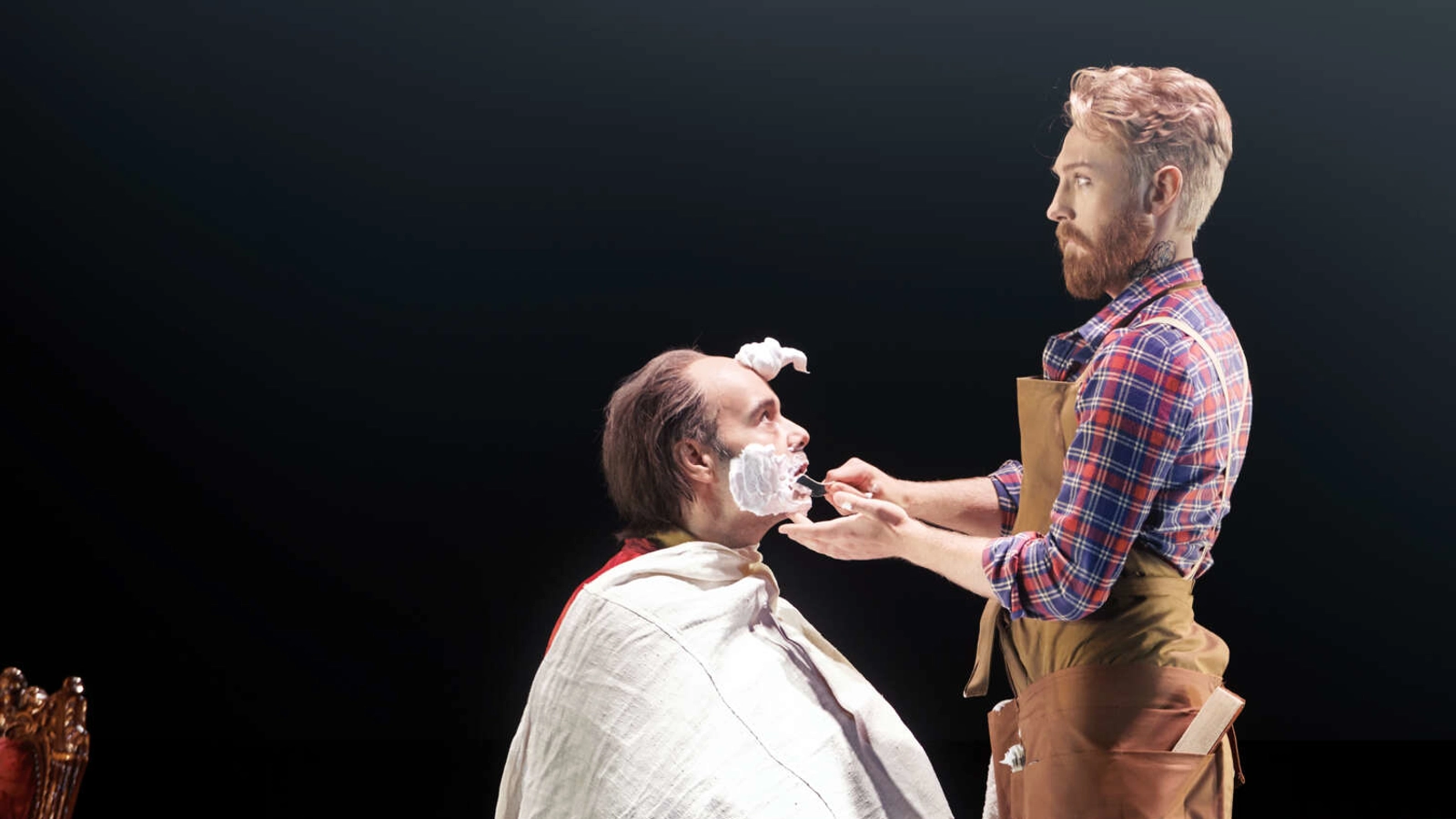 Figaro står framför Doktor Bartolo som sitter i en barberstol. Bartolo har raklödder på kinderna och en stor klick i pannan.