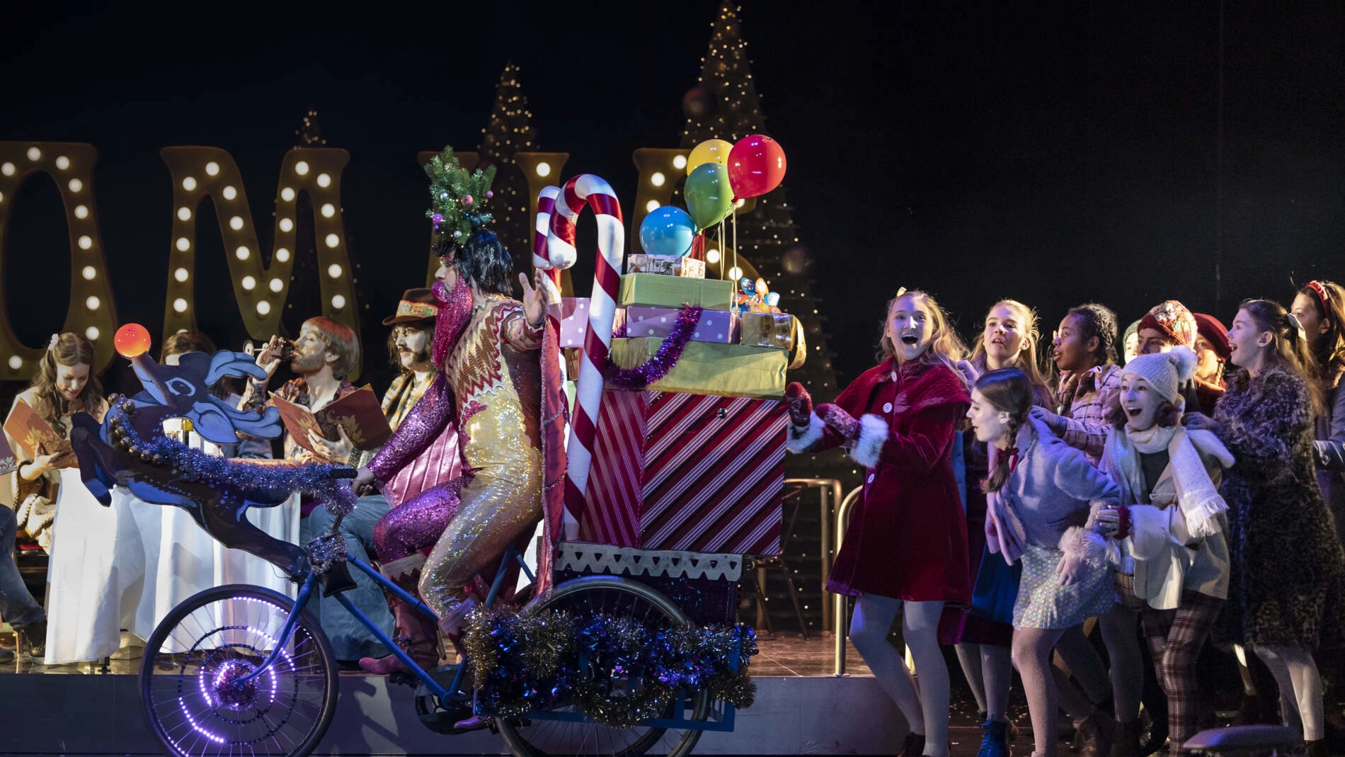 Parpignol cyklar in på en cykel lastad med julklappar, jagad av skrattande barn.