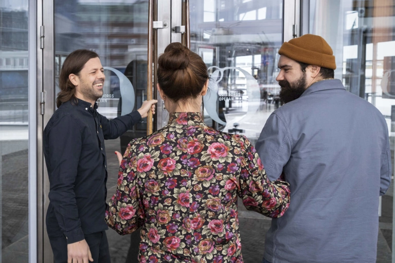 En person ler och är på väg att öppna glasdörrar för ett par som går i armkrok.