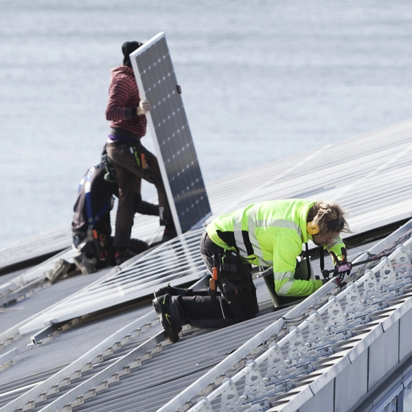 Tre tekniker installerar solpaneler på det sluttande taket på ett operahus.