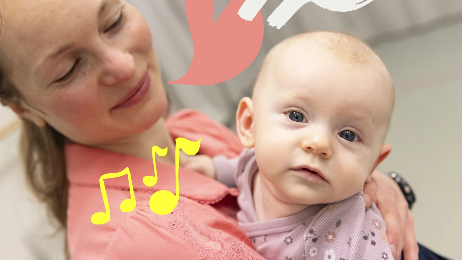 En ung bebis som hålls av sin mamma tittar rakt in i kameran. Hennes mamma tittar på henne och ler.