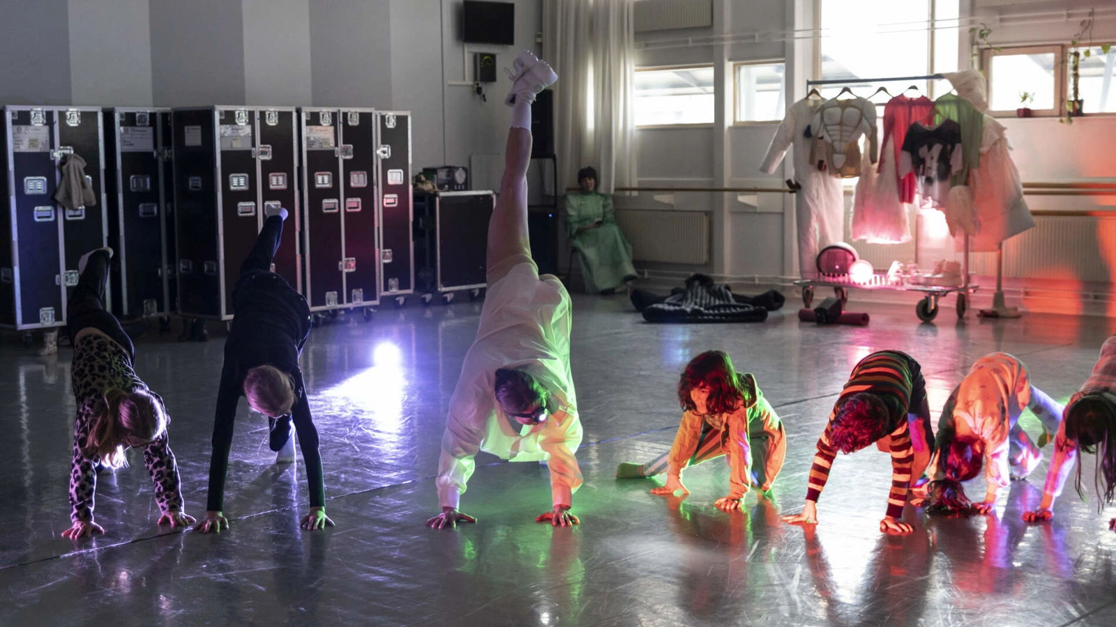 I en dansstudio en dansare med pannlampa lutar med händerna i golvet och ett ben höjt upp. Några barn försöker kopiera henne.
