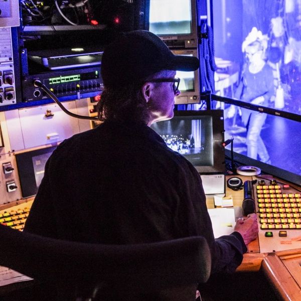 En inspicient sitter vid en kontrollpanel i båset vid sidan av en scen.